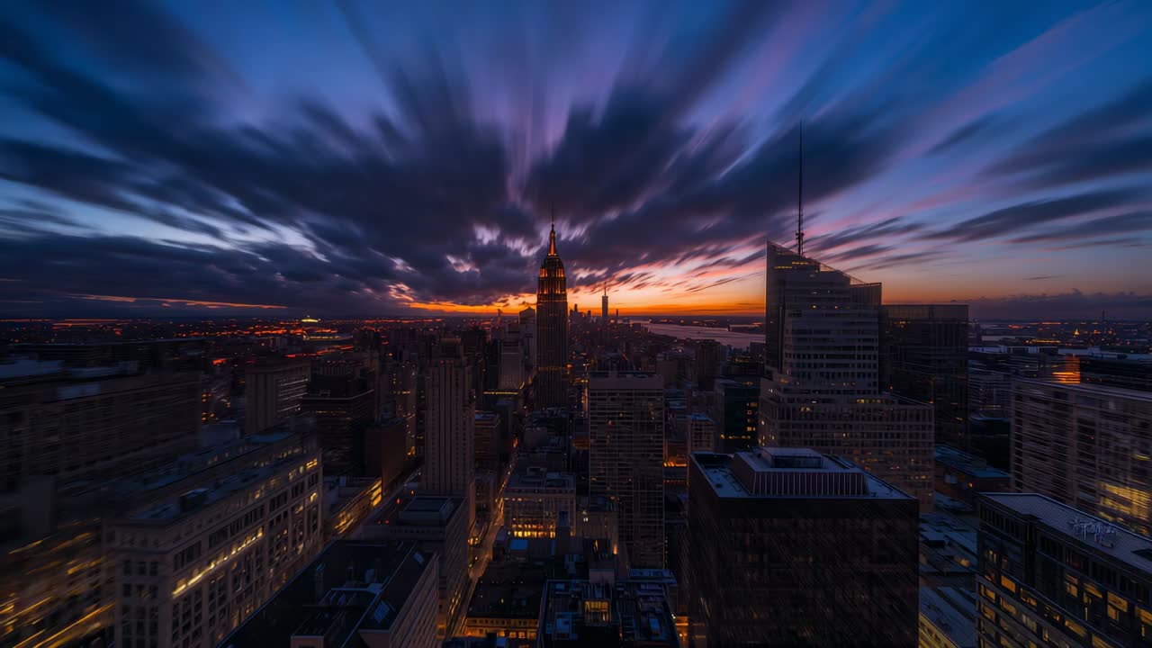 Showing city skyline and tower lighting up from rooftop as sun approaching horizon, windows glowing
