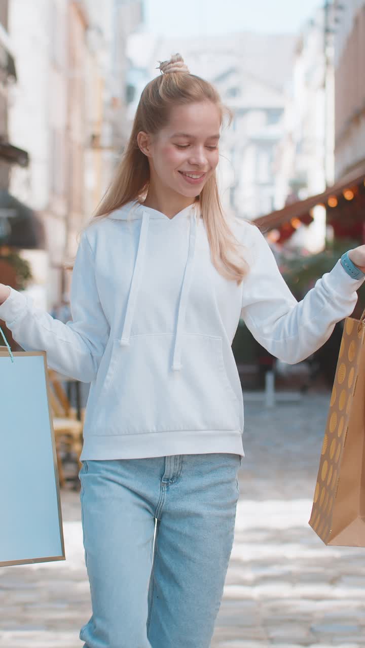 Happy smiling young caucasian woman shopaholic carrying shopping bags and walking on city street