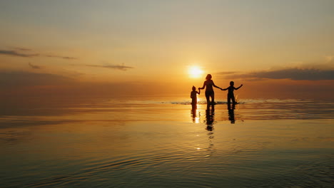 Mutter-Mit-Zwei-Kindern-Lachend-Im-Meer-Bei-Sonnenuntergang-Aus-Dem-Wasser