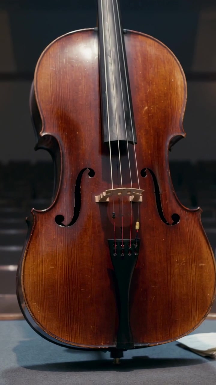 Video verticale: Telecamera in panoramica che rivela un violoncello sul palco, con tappeto imbottito, carta e sedute sfocate.