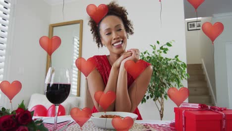 Animation-of-heart-balloons-over-african-american-woman-having-video-call-and-drinking-wine