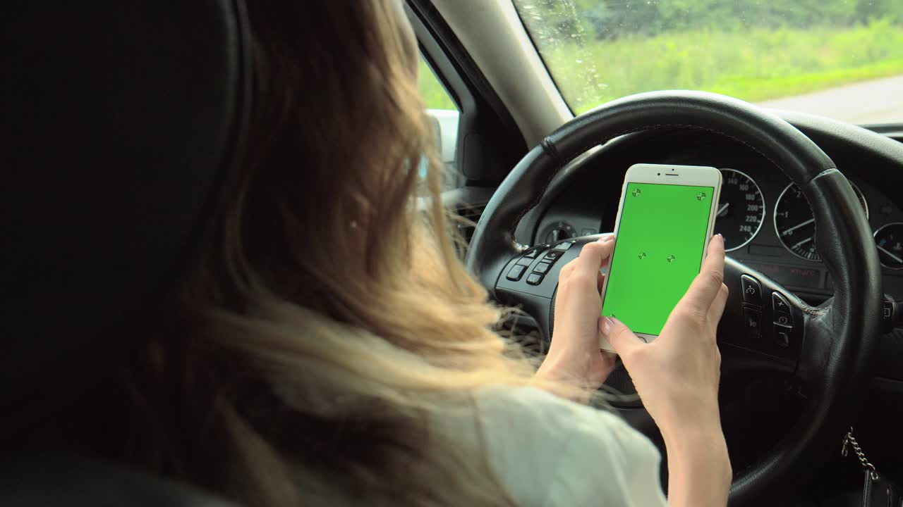 las manos de las mujeres sostienen un teléfono con una pantalla verde con las manos en el volante del coche. la chica conductor está sentada al volante sosteniendo un teléfono con un llave de croma en las manos