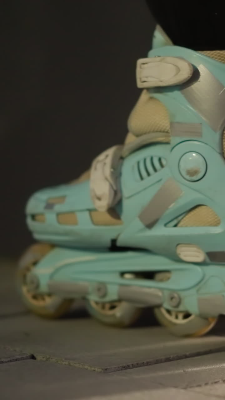 Side view of a pair of blue rollerblades gently rolling in place against a dark nighttime background. The scene highlights the smooth, controlled movement and the details of the rollerblades' design