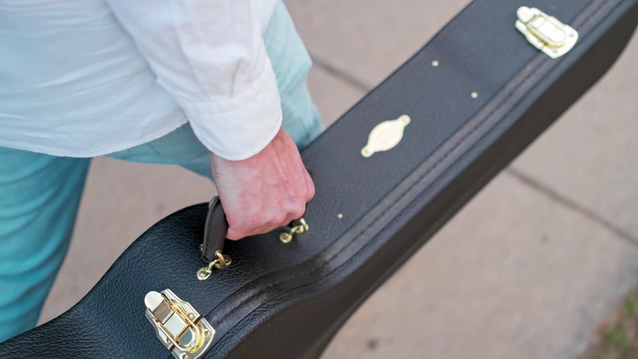 un guitarrista llevando un estuche de guitarra y caminando por la ciudad