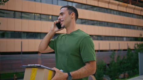 mail courier talking smartphone delivering package modern neighbourhood closeup