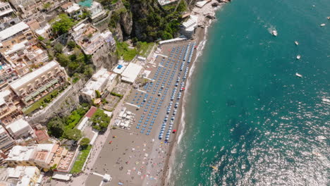 Toma-Aérea-De-La-Playa-De-Positano-En-La-Costa-De-Amalfi,-Italia-Con-Tumbonas-Y-Sombrillas.