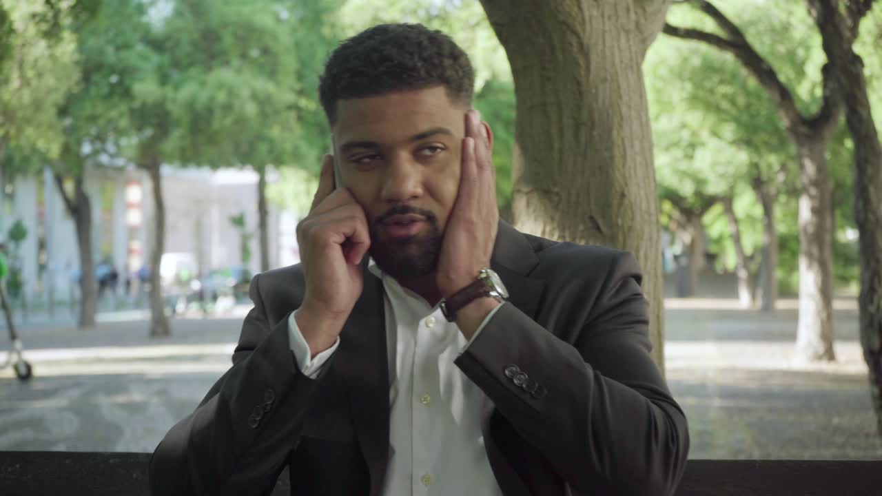 Tired businessman talking on smartphone in park.