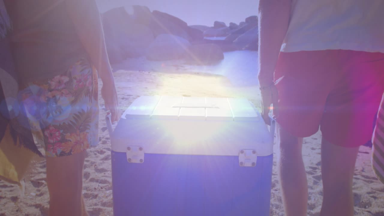 Due amici sollevano e trasportano una grande borsa frigo blu lungo la costa sabbiosa per una gita in spiaggia.