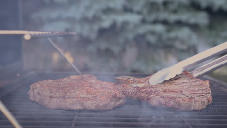 Side-view-of-juicy-steaks-sizzling-and-being-flipped-in-hot-flames