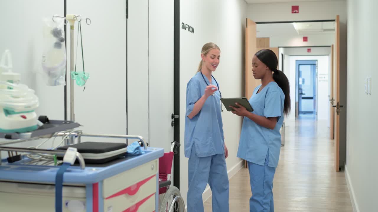 Diverse female nurses greeting and consulting on tablet while checking supply cart by staff room