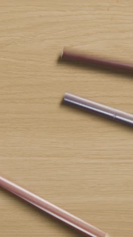 Vertical-Video-Of-Multi-Coloured-Pencils-Rolling-Down-Wooden-Background