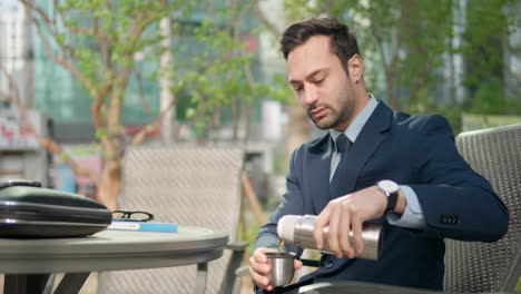 businessman drinking tea or coffee from steel thermos cup and enjoys lunch break at a city park