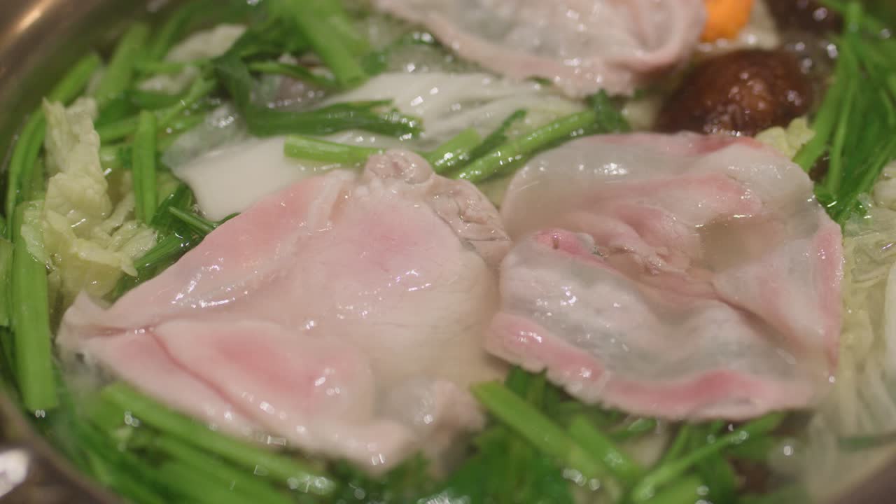 Chopsticks cook thin pork slices in bubbling hotpot with vegetables, under warm, even lighting