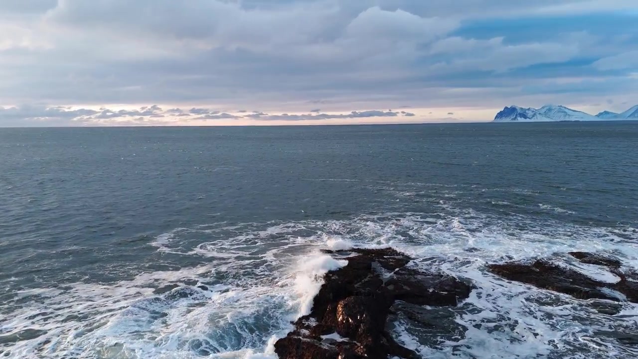 Luftfoto af kolde havbølger der slår mod sneklædte klipper