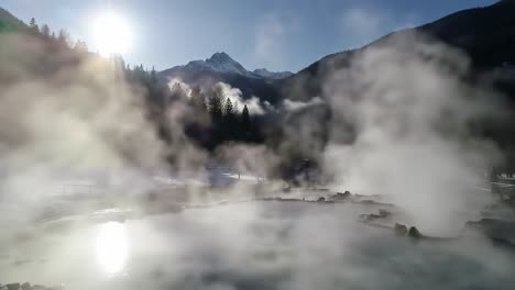 a serene morning at a natural hot springs with mist rising in the air under the early sunlight in a snowy mountain landscape
