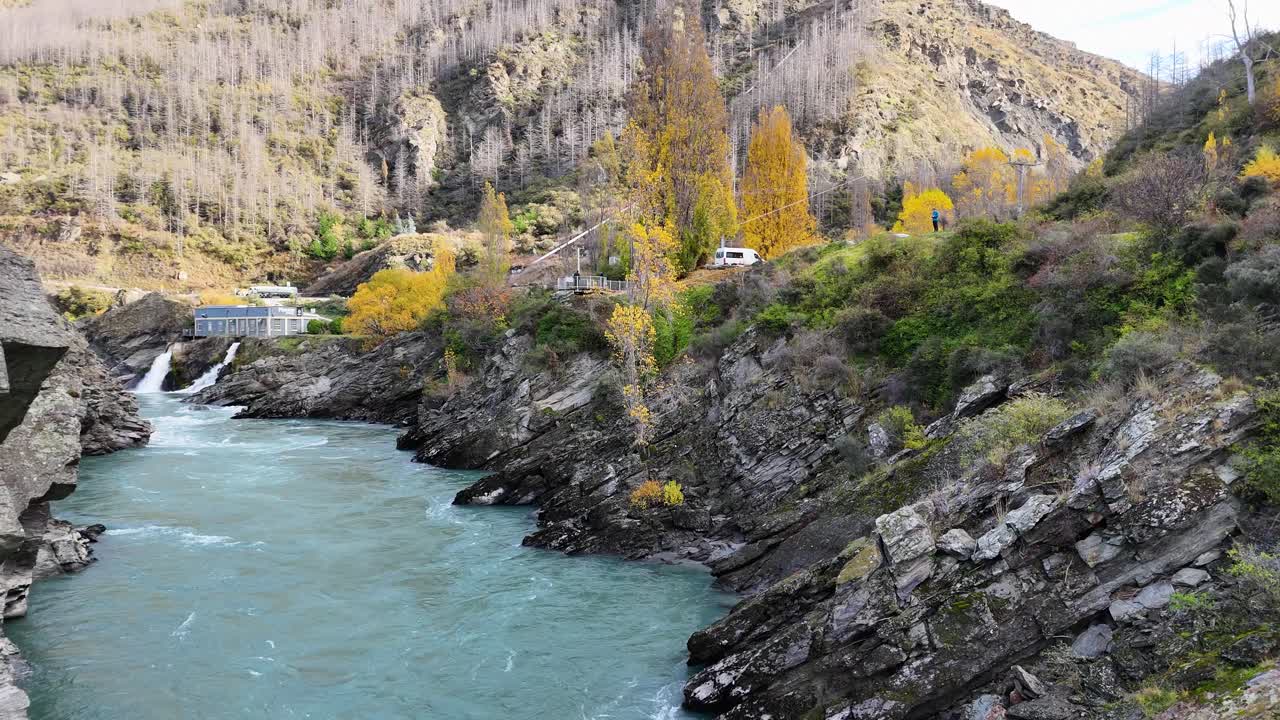 Aerial footage of Kawarau River in Queenstown, New Zealand, showcasing vibrant autumn foliage and a hydroelectric power station