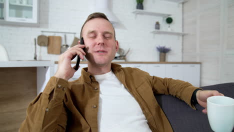 young man talking the phone at home. happy guy resting with a cup of coffee and having a pleasant phone conversationin the kitchen.