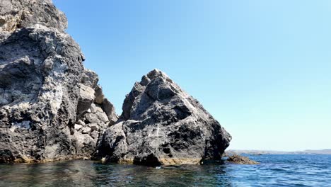 Two-large-rock-formations-on-the-coast-of-Sudak,-Crimea,-Russia,-with-clear-blue-water-and-a-bright-sky