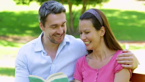 Happy-couple-sitting-on-a-park-bench-reading-together