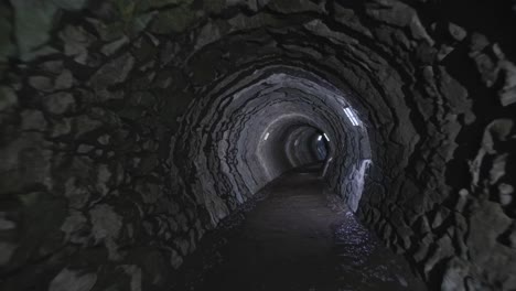 a dimly lit tunnel with rugged stone walls, captured from a first-person angle
