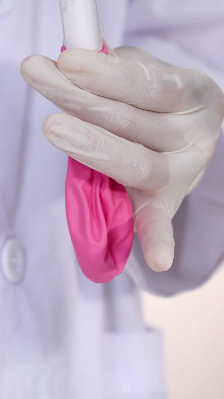 Primo piano verticale che mostra mani con guanti bianchi che preparano un palloncino rosa per un esperimento scientifico