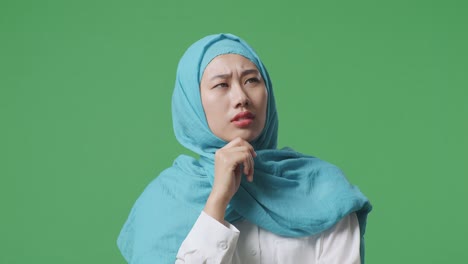 close up of asian muslim woman thinking and looking around then raising her index finger while standing in the green screen background studio