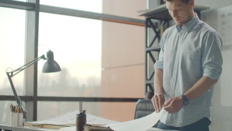 ingeniero hipster trabaja con planos. disparar desde arriba. joven ingeniero arquitectónico trabajando en la oficina. hombre barbudo hace bocetos. estilo loft dibujos interiores minimalistas en la mesa