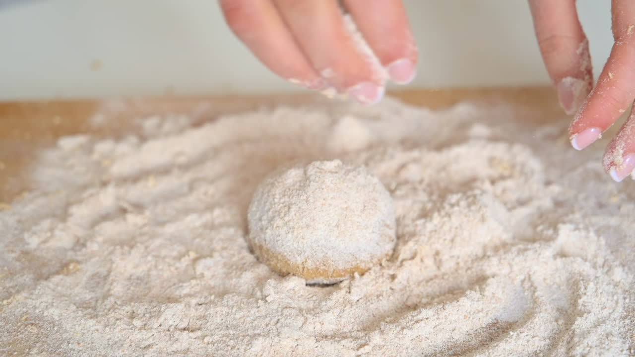 Woman wearing an apron, adding flour to dough on a wooden cutting board in the kitchen