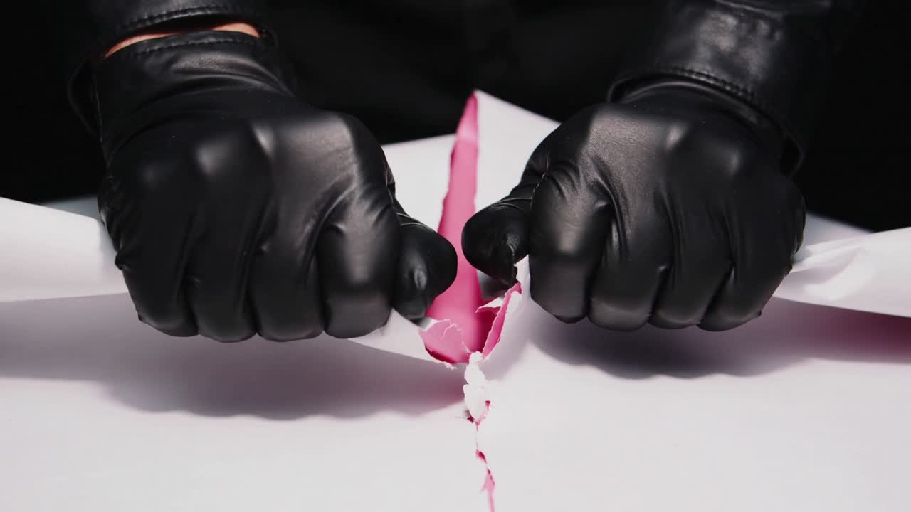 Tirando guanti neri pre-strappati che strappano la carta arrotolata sul tavolo, mostrando l'interno rosa.