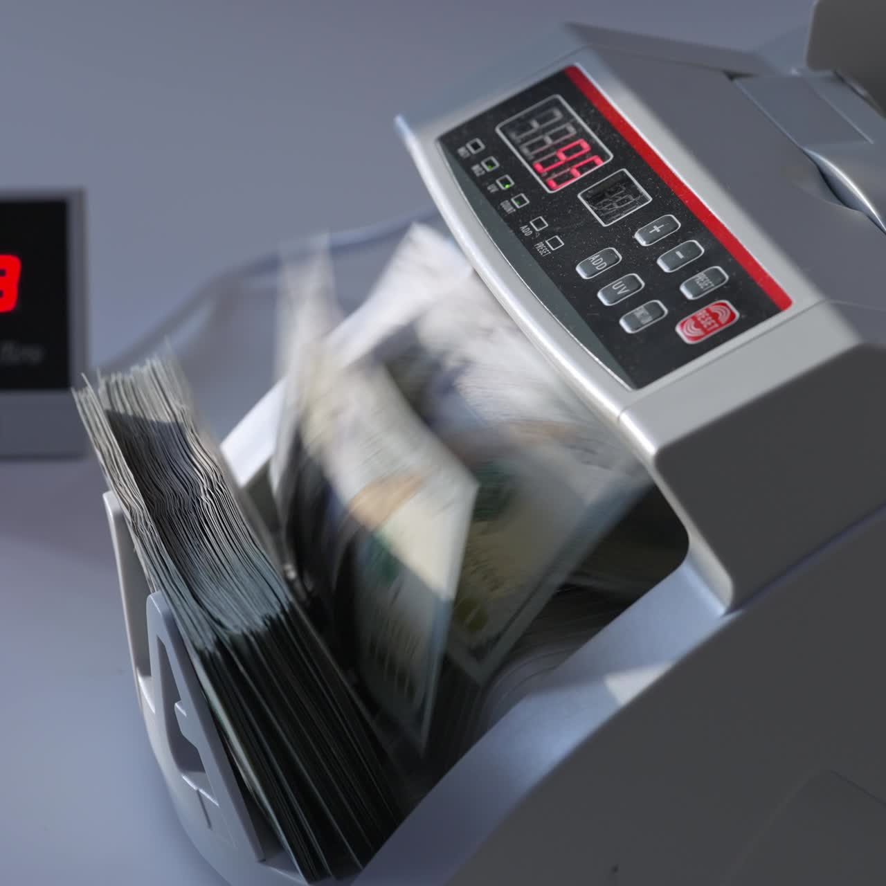 Man puts a big wad of hundred dollar notes into money counting machine. Side view. White background