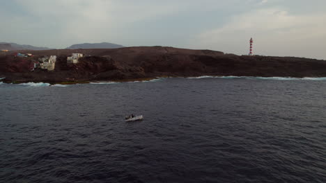 Exploring-the-North-Coast-of-Galdar,-Gran-Canaria:-Aerial-Views-of-Punta-de-Sardina-Lighthouse-and-boat-at-Sunset-