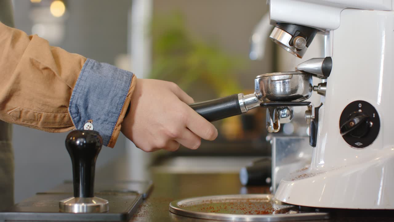 Barista pegando o porta-filtro no balcão do café, alinhando-o sob o cabeçote do grupo de café expresso para o preparo