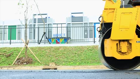 workers compact the asphalt using a rolling machine, tandem roller, which is a type of heavy compactor construction vehicle used to level soil, gravel, concrete or asphalt in road construction