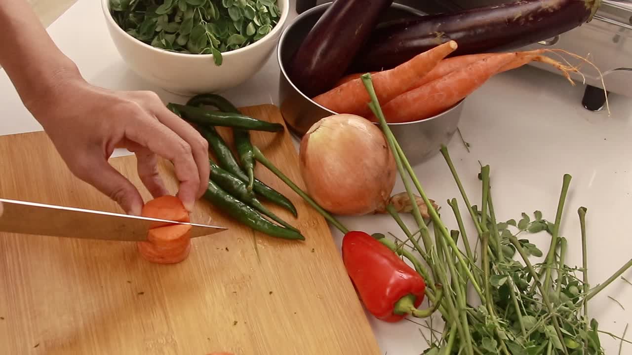 Overhead view of woman's hand slicing carrots into strips while preparing ingredients for cooking, candid moment of peaceful domestic home life