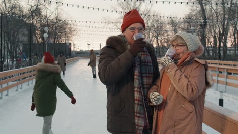 senior couple enjoying hot drinks at an outdoor ice skating rink