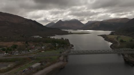 Toma-Aérea-En-Plataforma-Rodante-A-Lo-Largo-Del-Puente-De-Ballachulish-Con-Munros-Nevados-Al-Fondo