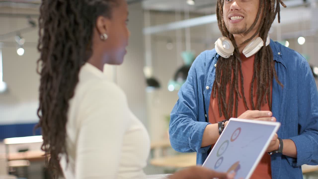 African American coworkers in office, woman holding white laptop explaining charts, man nodding