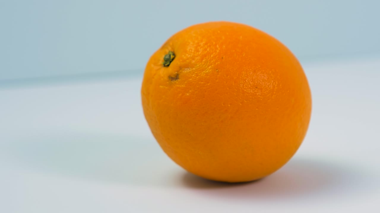 la naranja fresca, grande y jugosa gira lentamente sobre un fondo azul claro, concepto de comida saludable, primer plano extremo, cámara gira hacia la izquierda