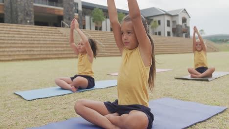 Video-of-focused-diverse-girls-practicing-yoga-on-mats-in-front-of-school