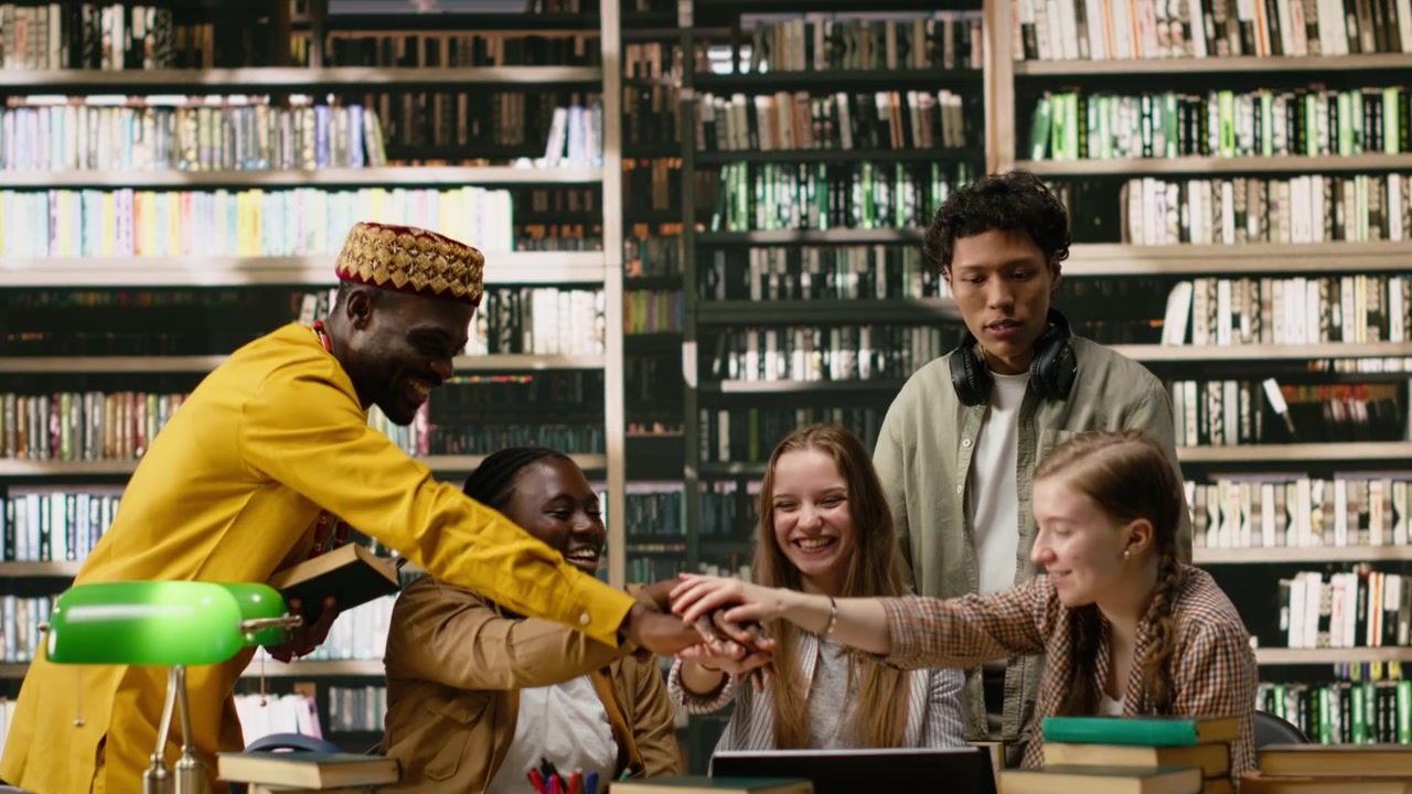 Students and adult learner uniting hands over library table after study session