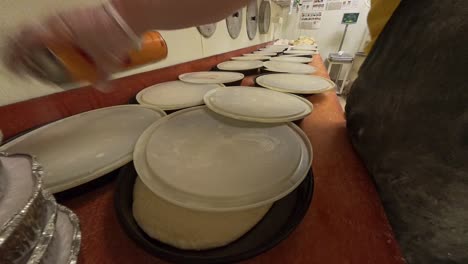 a worker spraying lids of raw pizza dough in cast iron pans.
