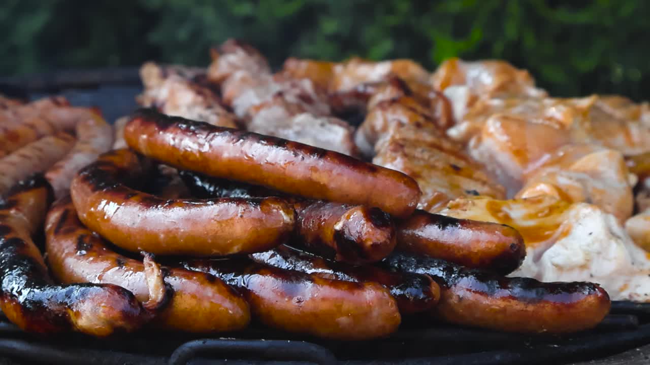 Gorgeous close up or closeup footage of golden brown and cooked sausages, chicken and meat being cooked on a barbecue grill in the summer time day while smoke is lifting up in slow motion, movement.