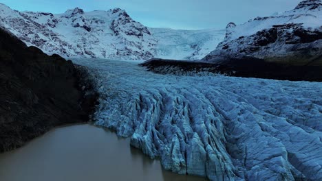 Vista-Aérea-Del-Glaciar-Svinafellsjokull-Con-Profundas-Grietas-En-Islandia-Rodeada-De-Montañas-Nevadas