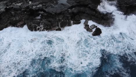 Deslizándose-A-Lo-Largo-De-Una-Costa-Volcánica-Desde-Arriba-Con-Acantilados-Negros-Y-Olas-Rompiendo