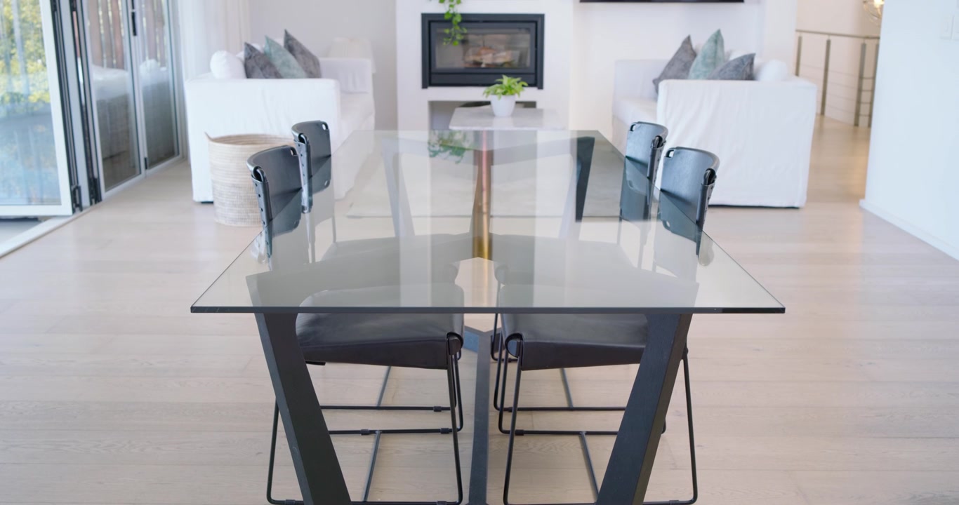 Camera pulling back glass-top table reflecting room and revealing sofas, fireplace to show layout