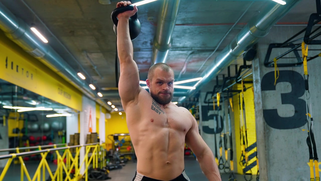 Uomo muscoloso che esegue una pressa sopra la testa con kettlebell a un braccio in palestra
