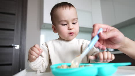 lovely baby licking his fingers during his meals. adorable toddler eating food from spoon his mom giving him. close up.