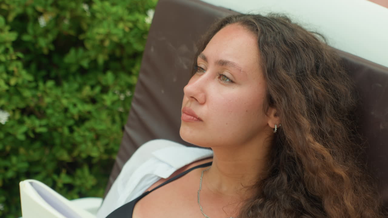 Uma senhora analisa a paisagem pensativamente. Mulher contemplativa com um caderno observa de perto os vibrantes arredores naturais. A senhora pensativa de cabelo encaracolado faz uma pausa para contemplar a vegetação exuberante à sua frente.