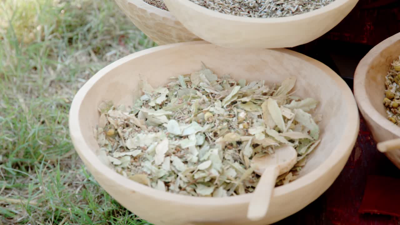 Close-up shot of three rustic wooden bowls overflowing with dried herbs, including large linden leaves and chamomile flowers, used for herbal tea or natural remedies