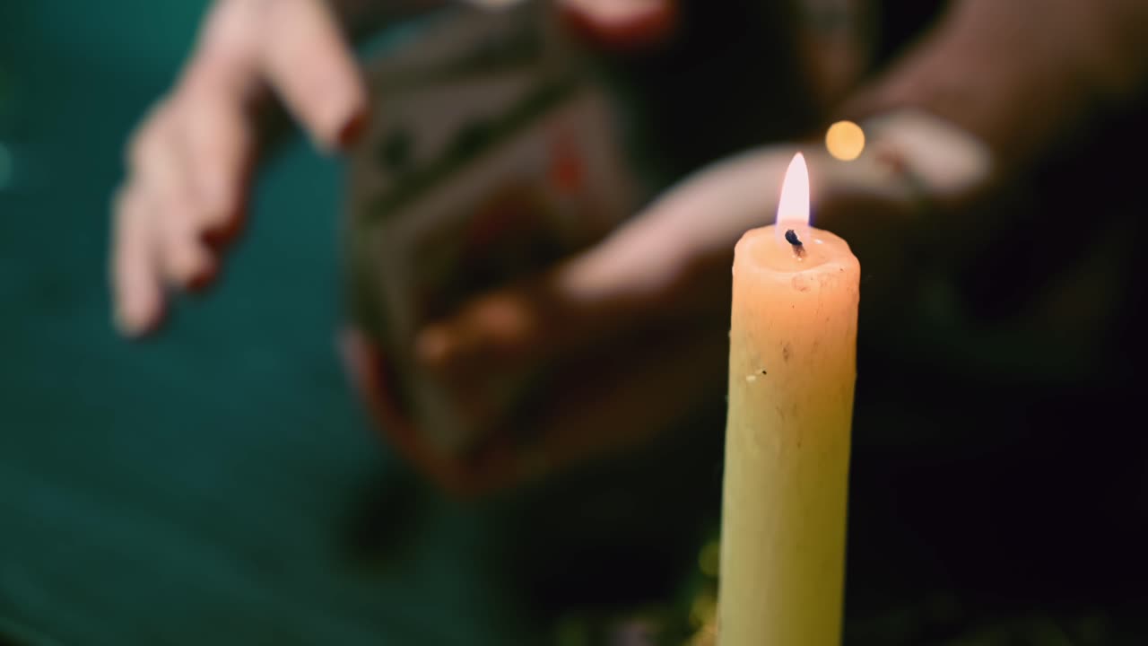 Fortune teller hands mix a card deck in background of a lit candle among mysterious esoteric jewelry. Overhead shot